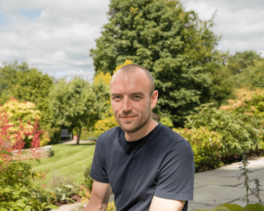 Andrew standing in garden with trees in the background